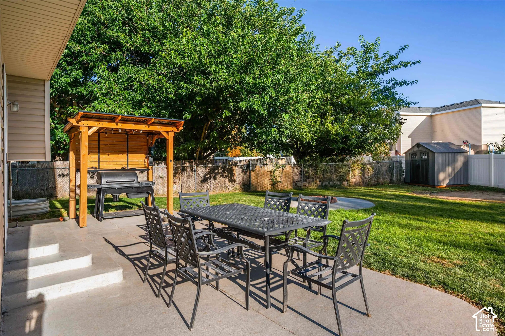 Concrete patio with steps, wood-framed outdoor cooking structure, expansive lawn, and a storage shed