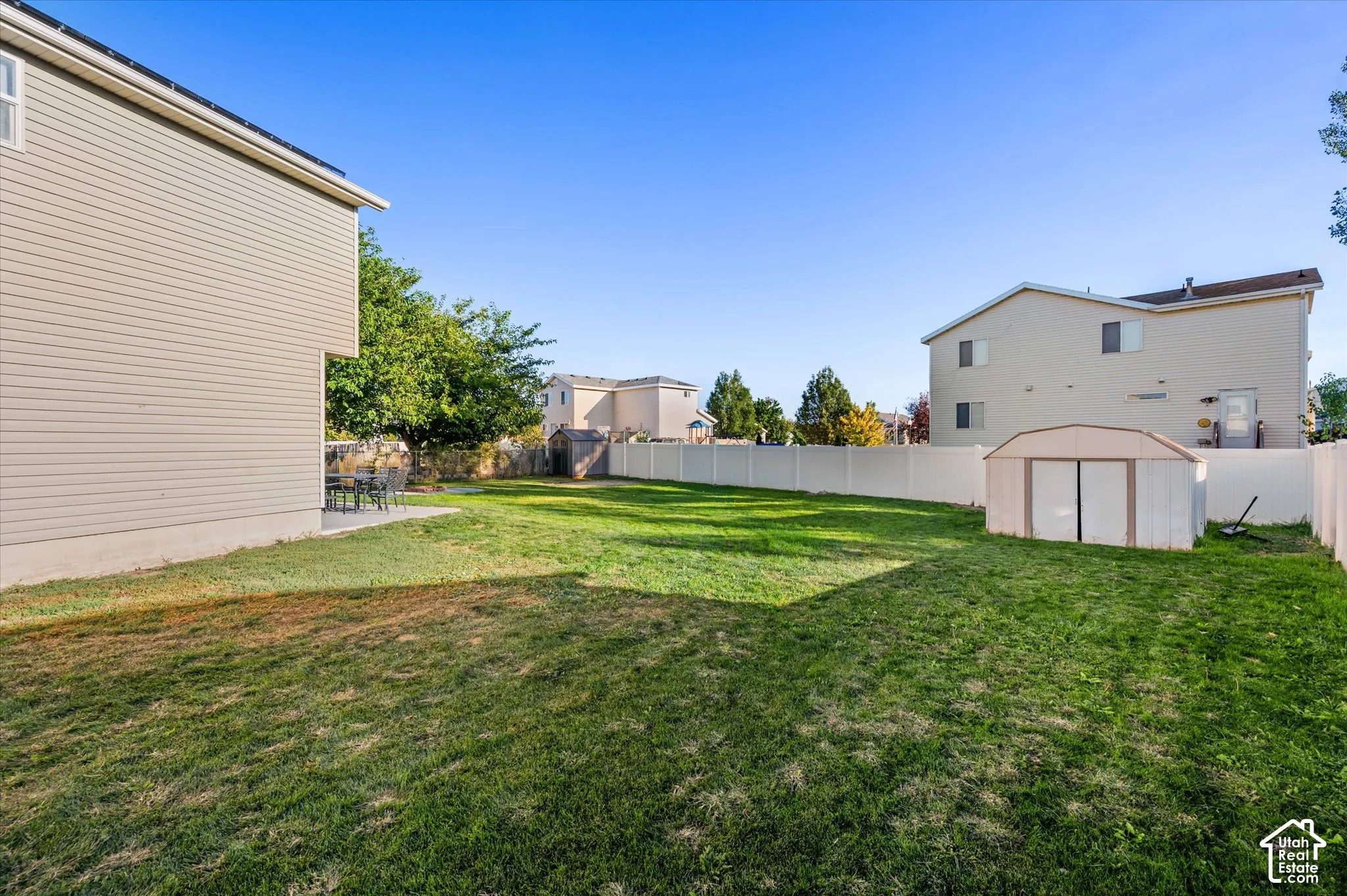 Expansive backyard featuring a large lawn, a white privacy fence, and a storage shed
