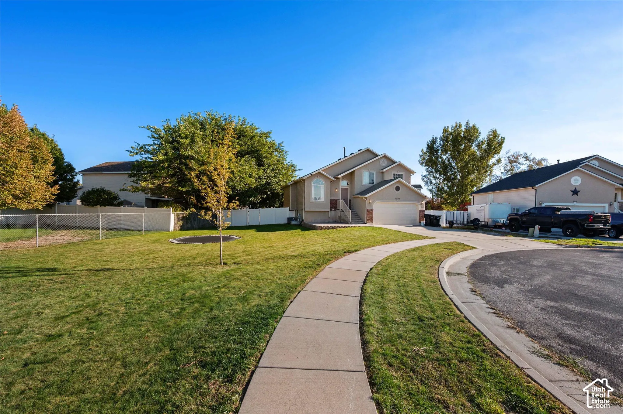 Two-story stucco exterior, attached garage, concrete driveway, front yard with mature trees, and a paved walkway