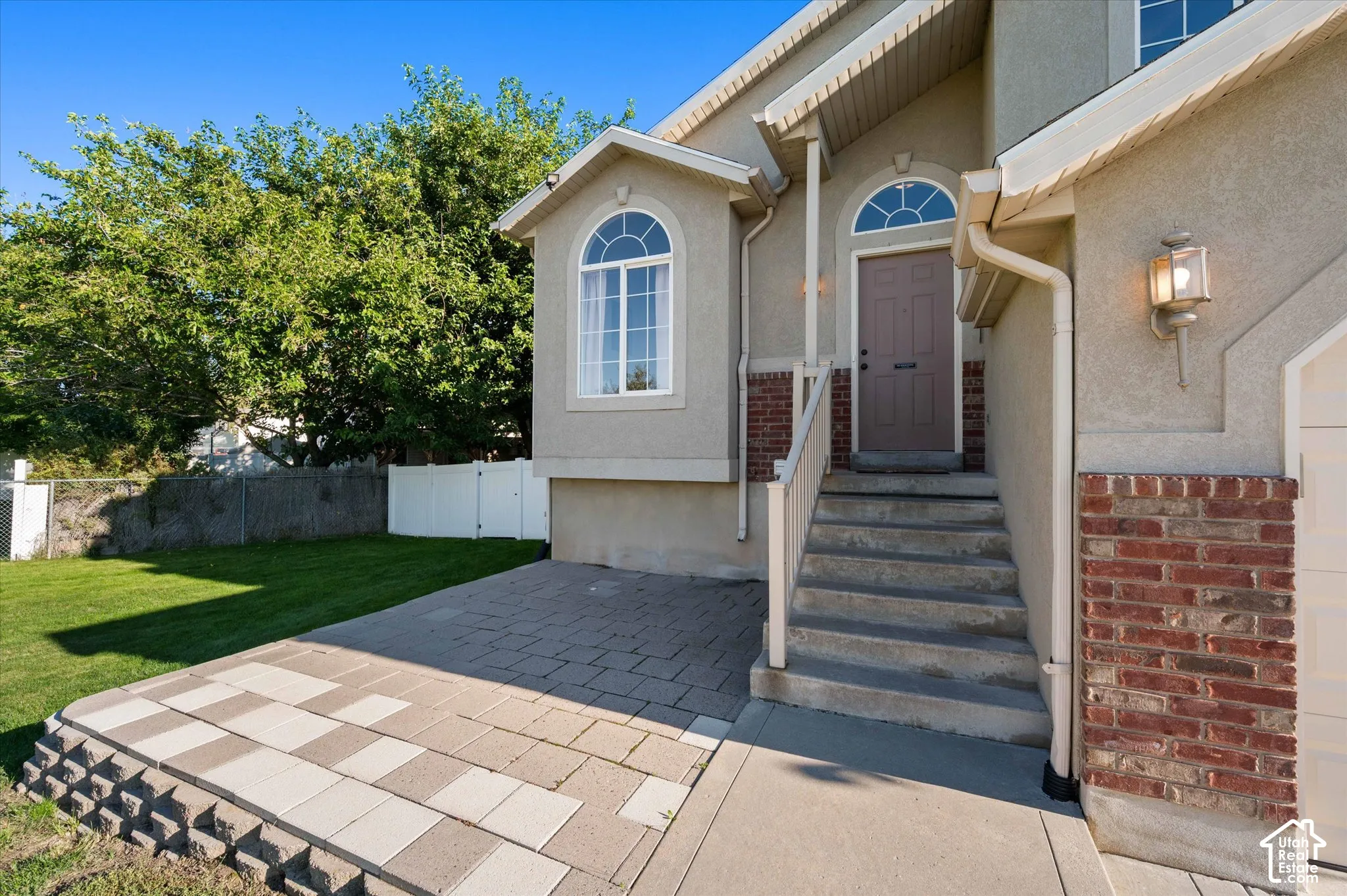 Stucco exterior with brick accents, arched window, exterior lighting fixture, concrete steps, and paver patio