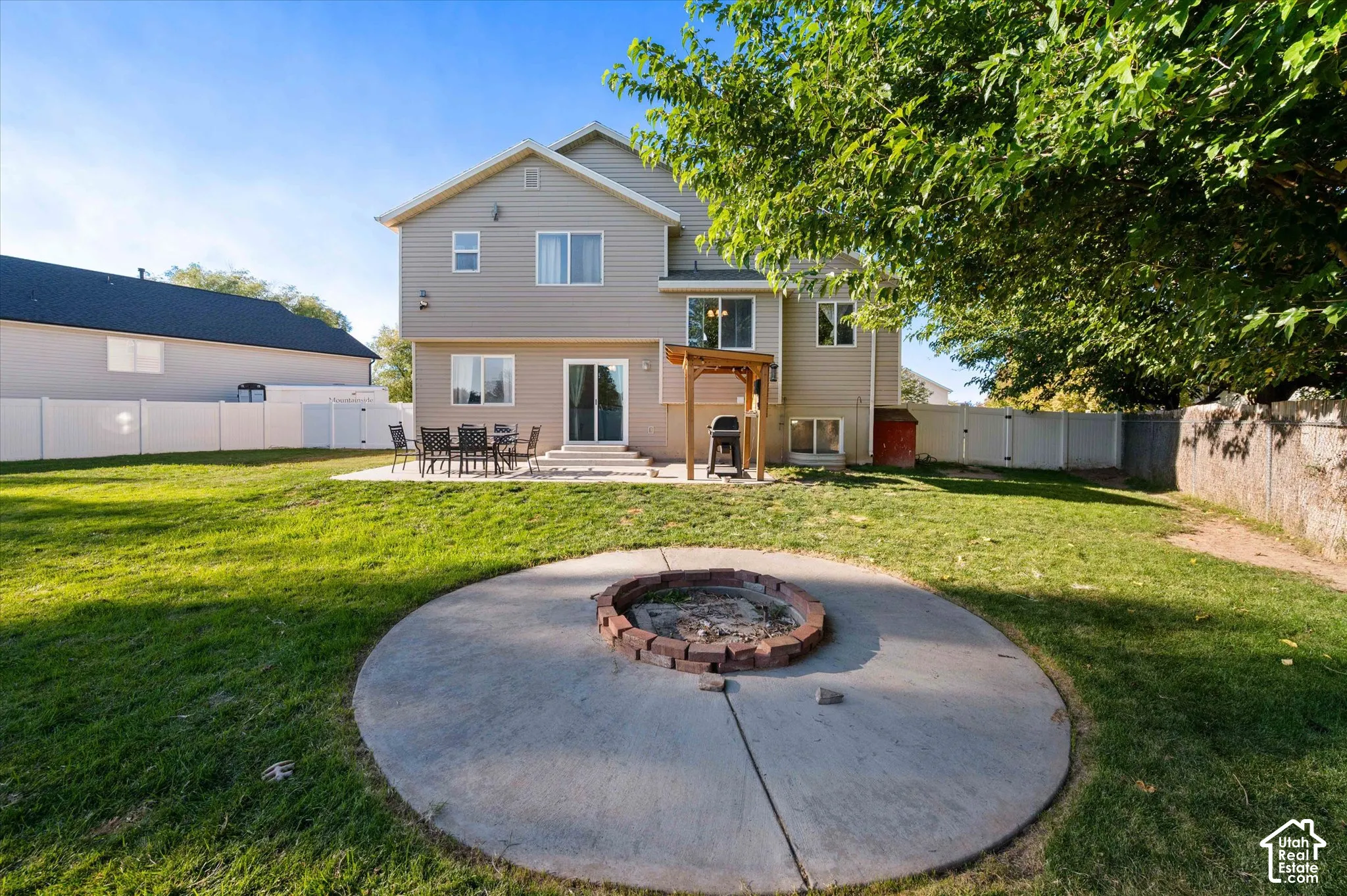 Expansive backyard featuring a concrete patio, built-in fire pit, and white privacy fencing