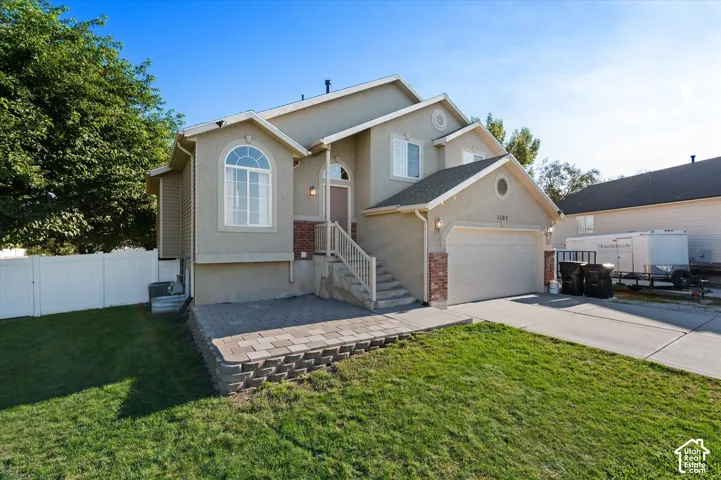 Stucco exterior with brick accents, arched windows, an attached garage, and a paver patio with a retaining wall