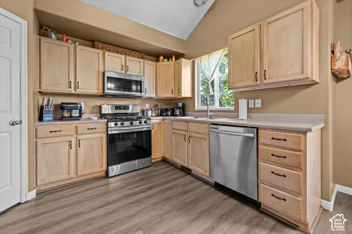 Kitchen featuring wood-finish flooring, light wood cabinetry, stainless steel appliances, and a vaulted ceiling