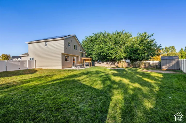 Spacious backyard featuring a manicured lawn, white vinyl fencing, a concrete patio, and a wood pergola