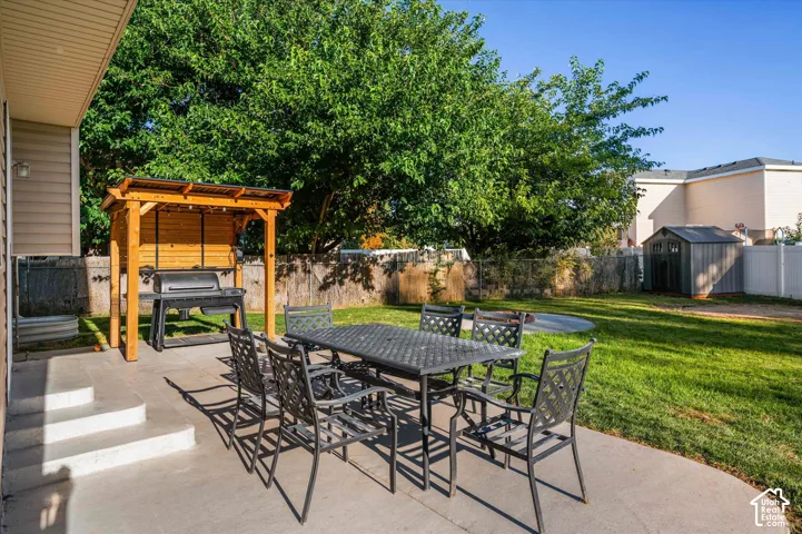 Concrete patio with steps, wood-framed outdoor cooking structure, expansive lawn, and a storage shed