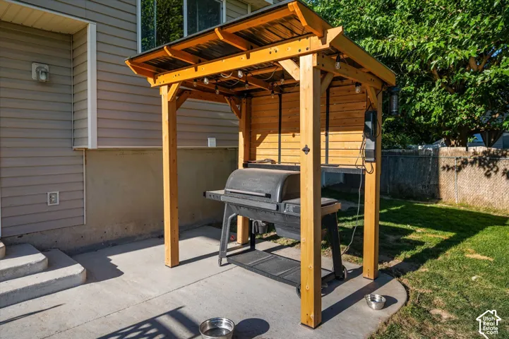 Outdoor grilling station featuring a wood-finish pergola with string lighting, concrete patio, and mature trees beyond