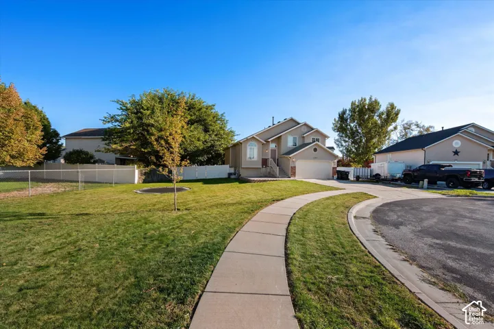 Two-story stucco exterior, attached garage, concrete driveway, front yard with mature trees, and a paved walkway