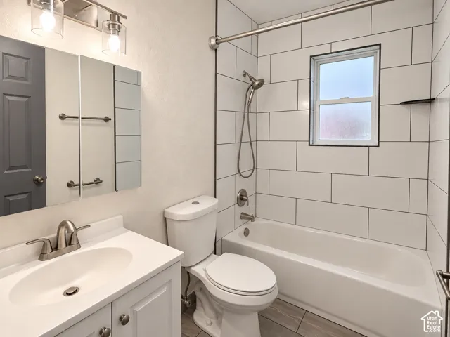 White subway tile shower surround, brushed nickel fixtures, white vanity with integrated sink, rectangular medicine cabinet, and grey wood-finish flooring