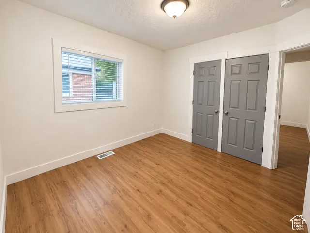 Wood-finish flooring, neutral wall paint, white trim, and gray paneled closet doors