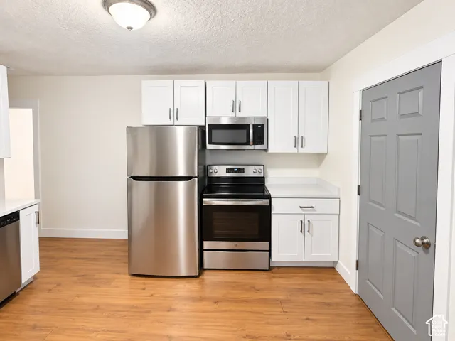 Kitchen featuring wood-finish flooring, white cabinetry, stainless steel appliances, and light-colored countertops