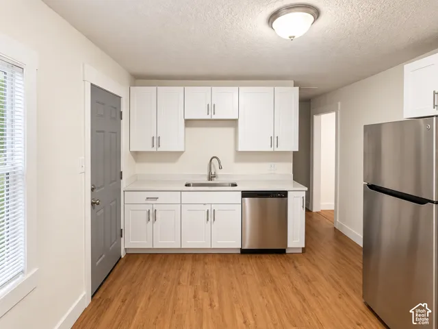 White cabinetry, stainless steel appliances, wood-finish flooring, white countertops, and a ceiling-mounted light fixture