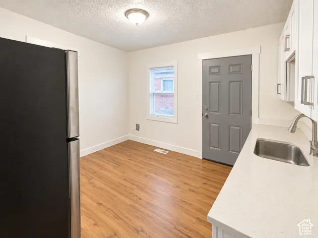 Wood-finish flooring, white cabinetry with silver-tone pulls, stainless steel sink with gooseneck faucet, light-toned countertop, and recessed ceiling light fixture