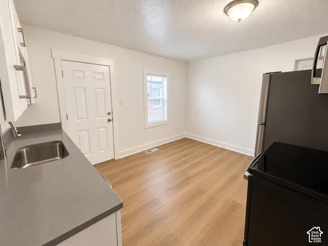 Kitchen featuring wood-finish flooring, white cabinetry with silver hardware, an undermount stainless steel sink, and gray countertops