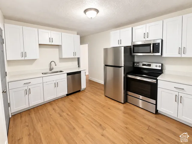 Well-appointed kitchen featuring white cabinetry, stainless steel appliances, light-toned countertops, and wood-finish flooring
