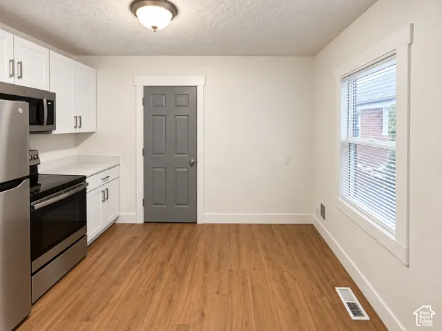 Kitchen featuring white cabinetry, stainless steel appliances, wood-finish flooring, and a window with blinds