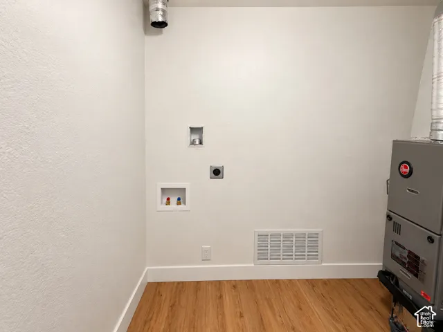 Wood-finish flooring with white baseboards, utility hookups, and a forced-air furnace