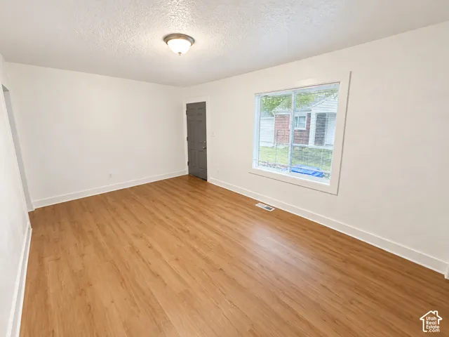 Spacious room with wood-finish flooring, white walls, and a large window