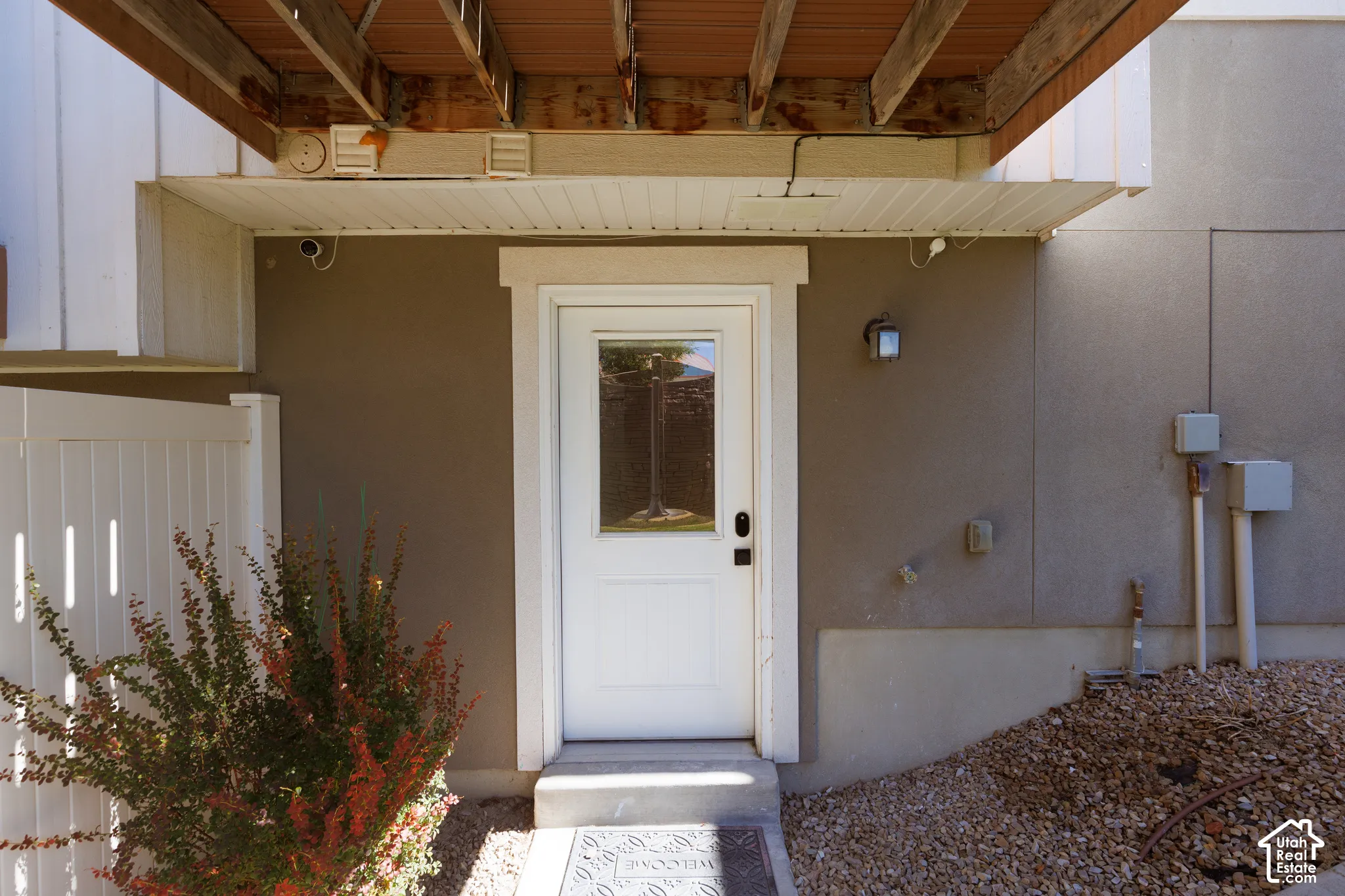 Entry door with transom window, exterior wall light, and an overhead awning