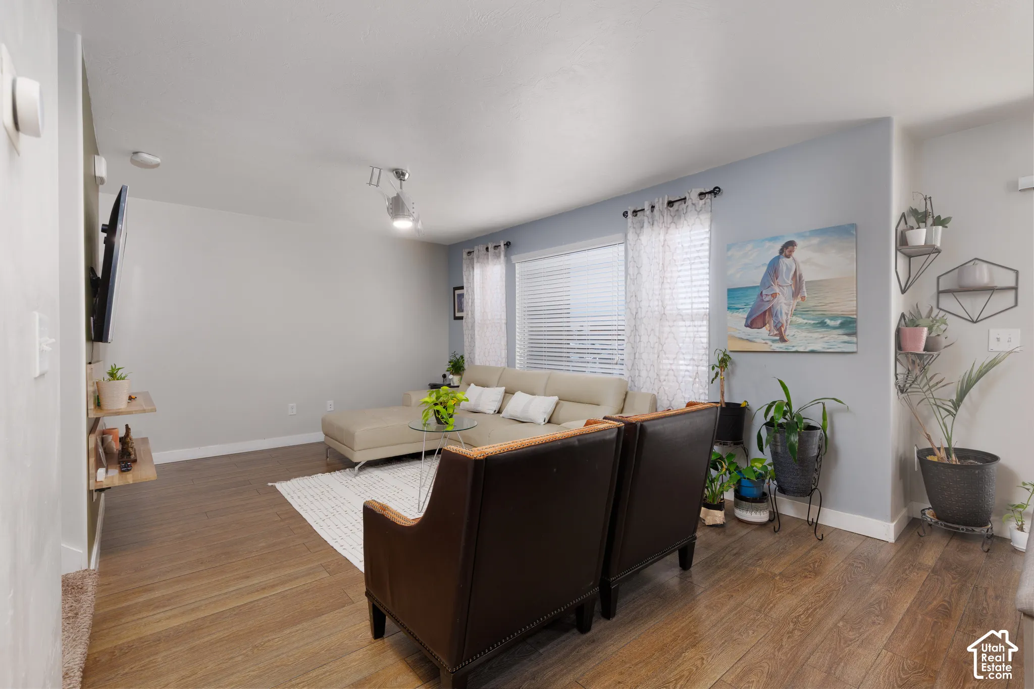 Spacious room featuring wood-finish flooring, light-toned walls, track lighting, and a large window with blinds
