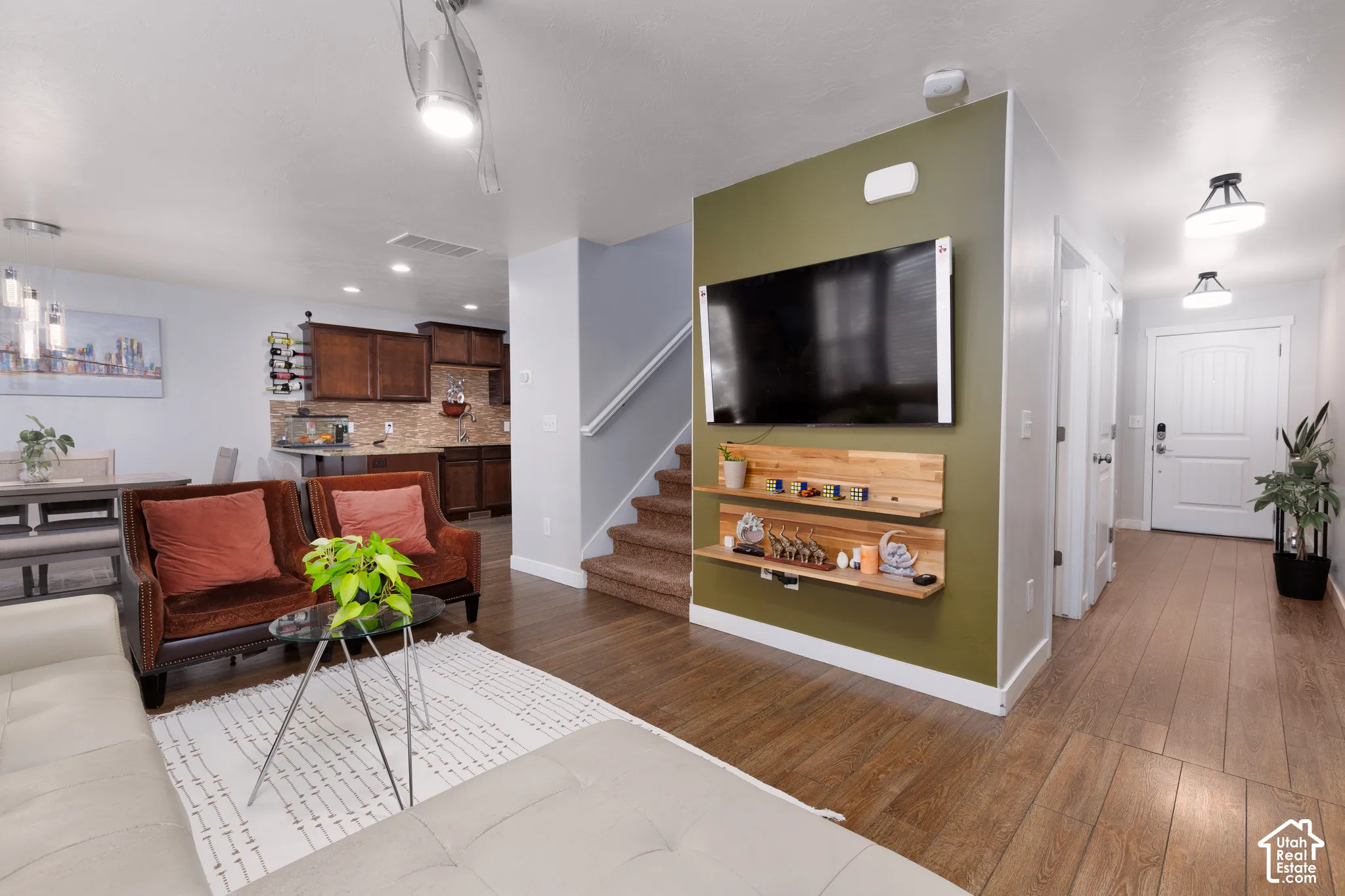 Wood-finish flooring throughout, modern ceiling fan, recessed lighting, built-in shelving, and a prominent media wall