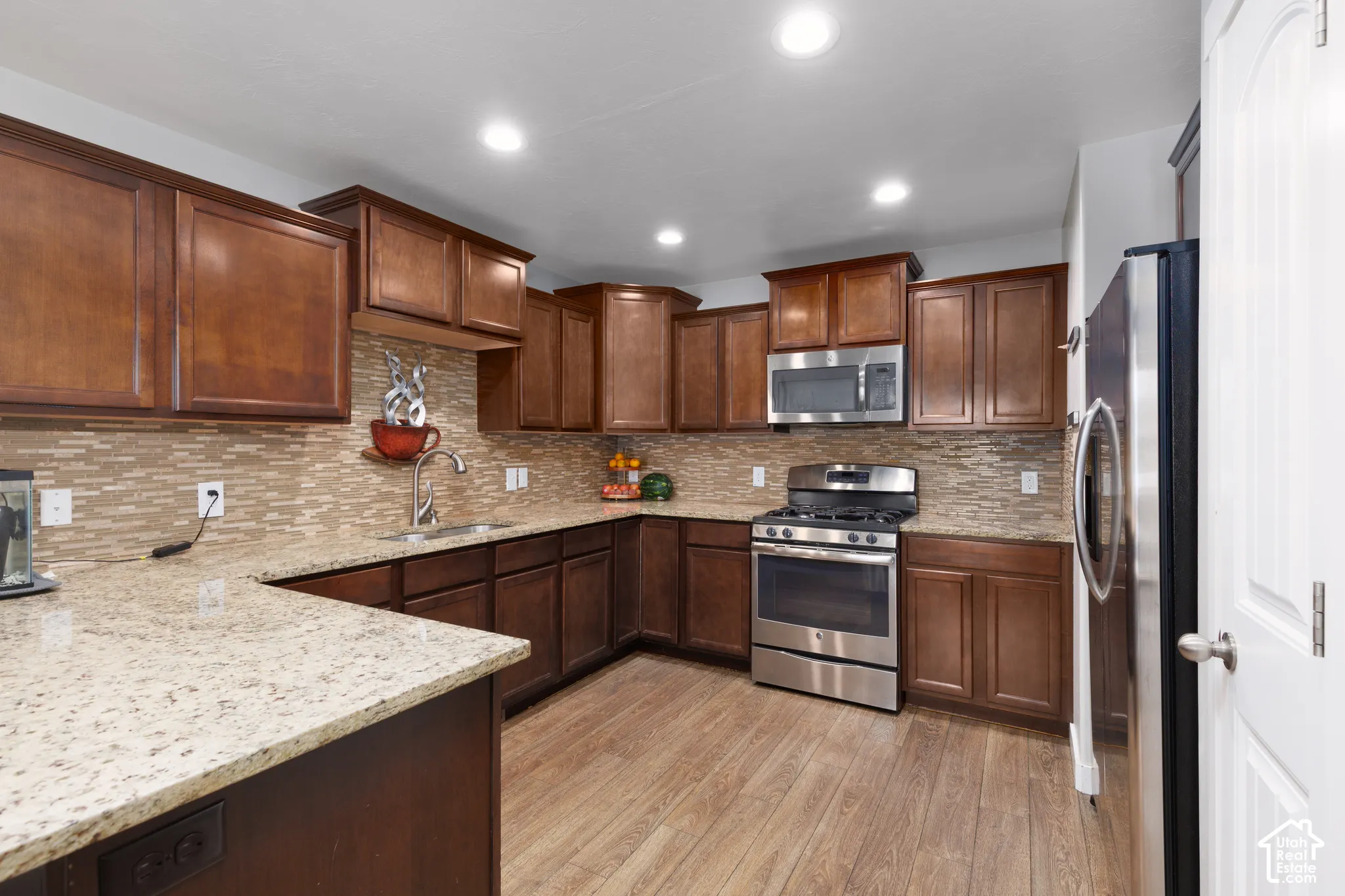 Kitchen featuring rich wood cabinetry, granite countertops, a mosaic tile backsplash, stainless steel appliances, and wood-finish flooring