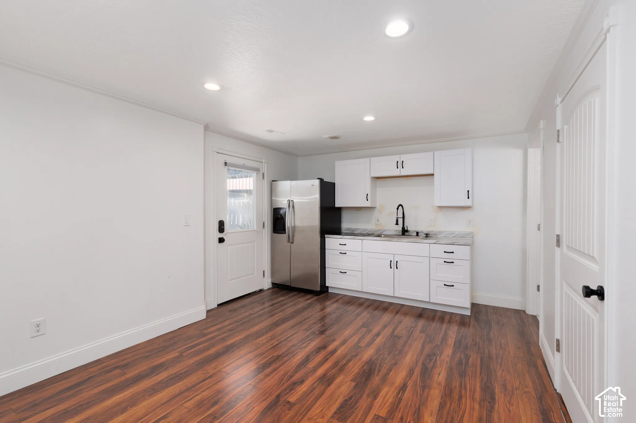 Modern kitchen space featuring white cabinetry, stainless steel refrigerator, dark wood-finish flooring, and recessed lighting