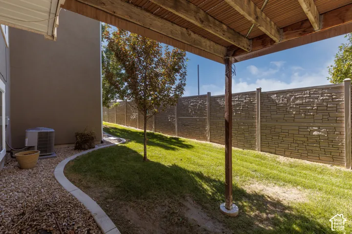 Landscaped exterior featuring a stone-pattern fence, graded lawn, mature tree, and gravel-edged pathway
