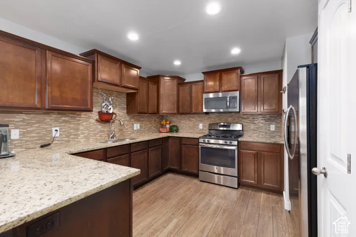 Kitchen featuring rich wood cabinetry, granite countertops, a mosaic tile backsplash, stainless steel appliances, and wood-finish flooring