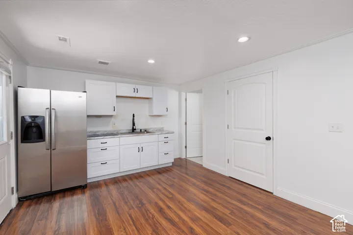 White cabinetry with matte black hardware, stainless steel refrigerator, dark wood-finish flooring, and recessed lighting