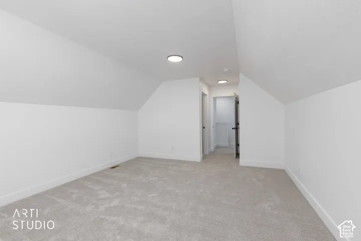 Recessed lighting, sloped ceiling, light-toned carpeting, white walls, and a white baseboard trim