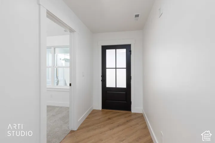 Wood-finish flooring, white walls, black interior door with frosted glass panels, white trim, and recessed lighting