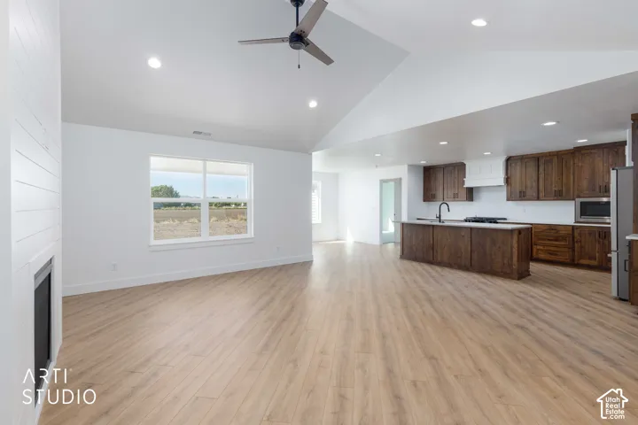Vaulted ceilings with recessed lighting, wood-finish flooring, white shiplap fireplace surround, wood cabinetry, and a kitchen island with sink
