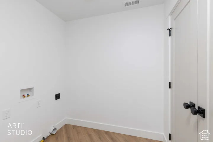 Dedicated laundry area featuring a white utility box, wood-finish flooring, and a white door with matte black hardware