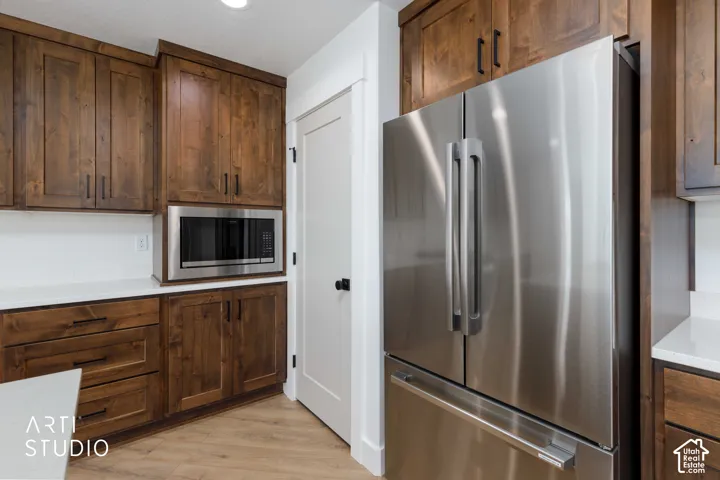 Stainless steel French door refrigerator, built-in microwave, wood-finish cabinetry, white countertops, and light wood-finish flooring
