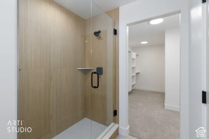 Glass-enclosed shower with wood-finish wall tile, a black shower head, and a corner shelf