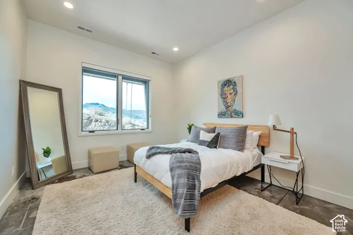 Recessed lighting illuminates concrete-finish flooring with a light wood-tone bed frame and a white nightstand