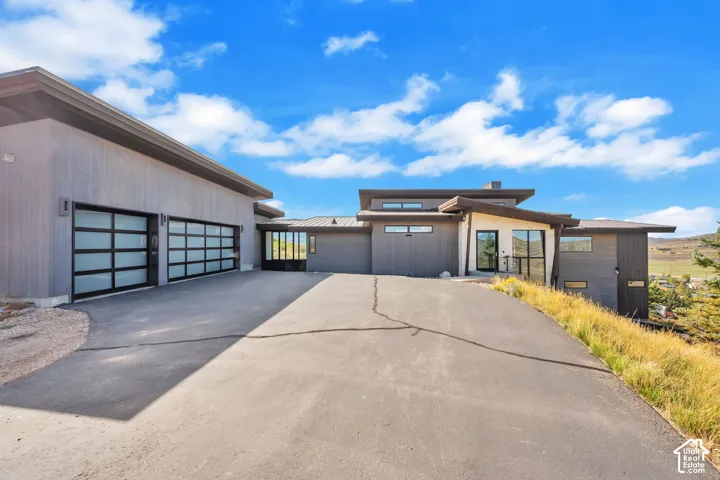 Modern architectural design featuring multi-level construction, a paved driveway, and multiple glass-paneled garage doors