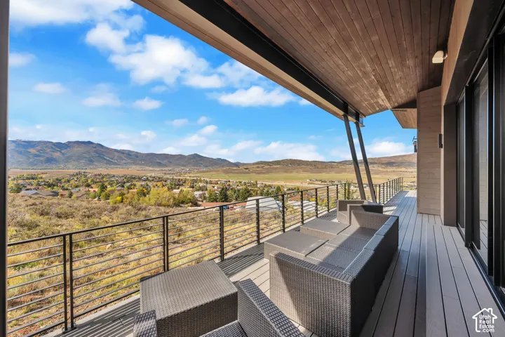Expansive covered deck with modern horizontal cable railing, composite decking, and built-in seating areas overlooking panoramic mountain and valley landscapes