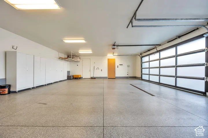 Spacious garage featuring polished concrete flooring, overhead LED lighting, built-in cabinetry along the perimeter, and a modern glass garage door panel system allowing natural light throughout the interior