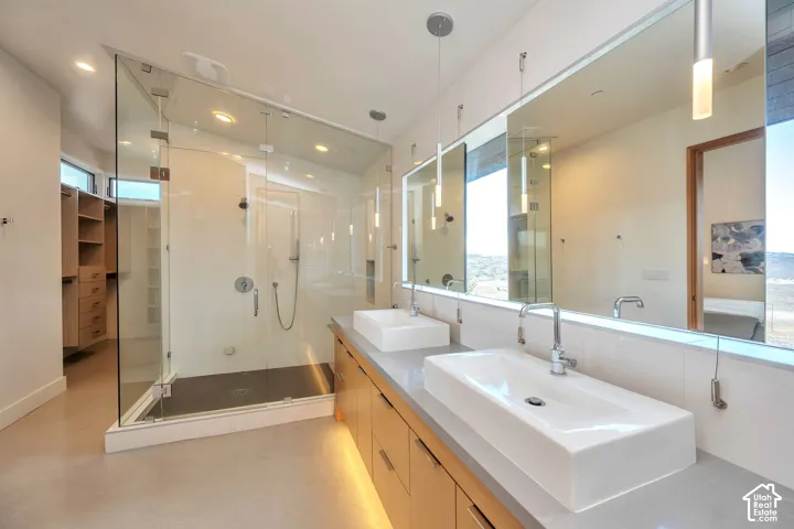 Dual rectangular vessel sinks, extensive vanity with wood-finish cabinetry, frameless glass shower enclosure, built-in shelving, and reflective surfaces