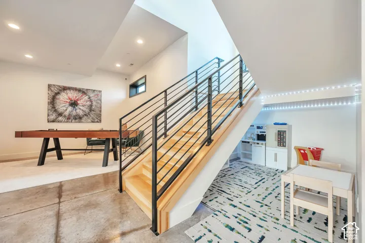 Modern open-concept interior showcasing a floating staircase with horizontal metal railings and natural wood treads, polished concrete flooring, and recessed ceiling lighting