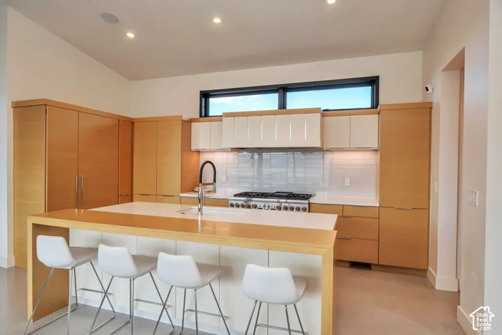 Modern kitchen featuring light wood-finish cabinetry, white countertop, tile backsplash, and a large central island