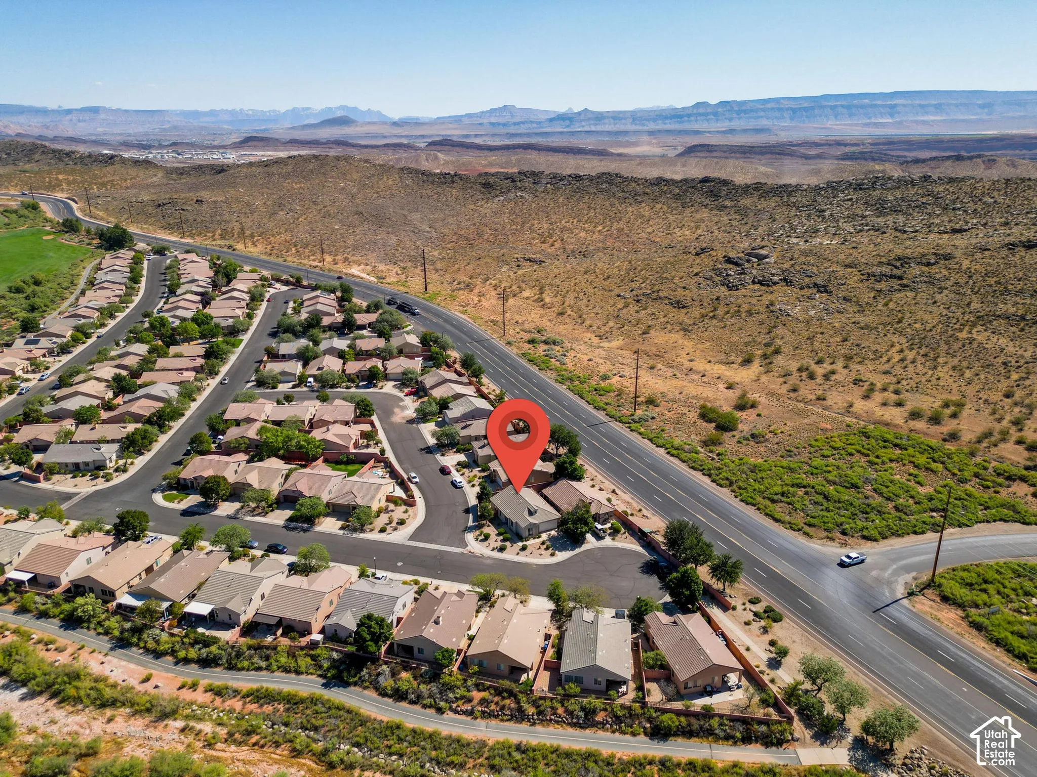 Residential community with paved roads and mature landscaping, bordered by undeveloped desert terrain and distant mountains