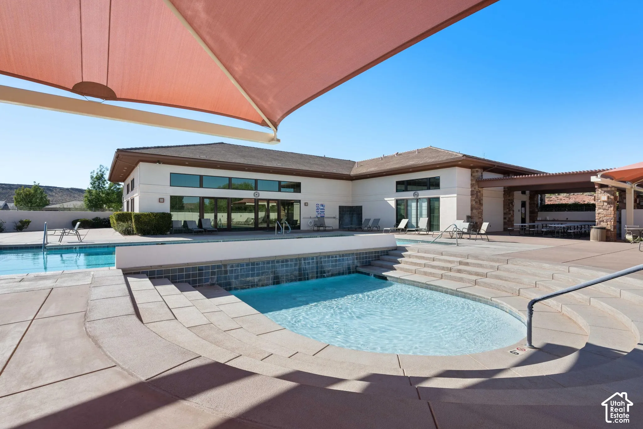 Outdoor pool area featuring a large spa with waterfall, integrated steps, and a surrounding paved deck