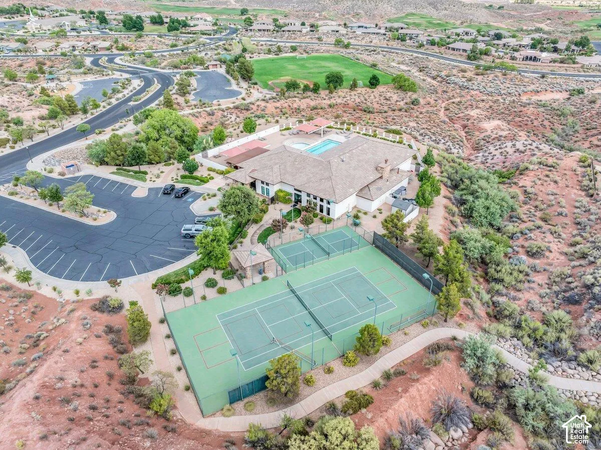Expansive community building featuring a swimming pool, two tennis courts, and a large parking area, surrounded by desert landscaping and winding pathways