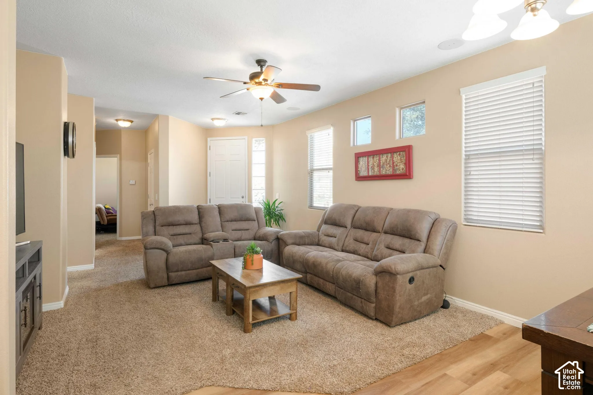 Neutral tone wall paint, recessed lighting, ceiling fan, multiple windows with blinds, and a combination of carpet and wood-finish flooring