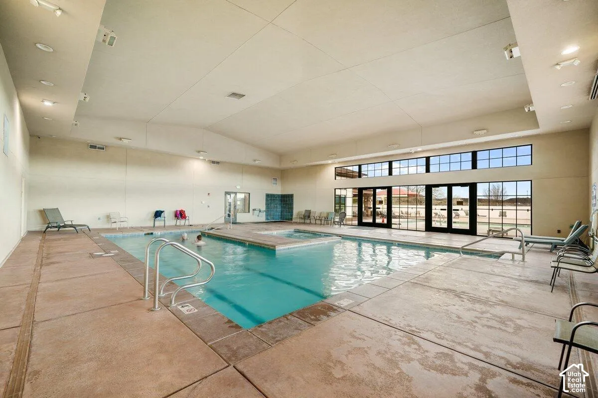 Indoor swimming pool with an integrated spa, expansive floor-to-ceiling windows, and abundant recessed lighting