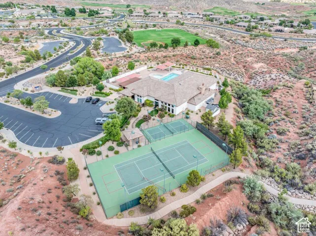 Expansive community building featuring a swimming pool, two tennis courts, and a large parking area, surrounded by desert landscaping and winding pathways