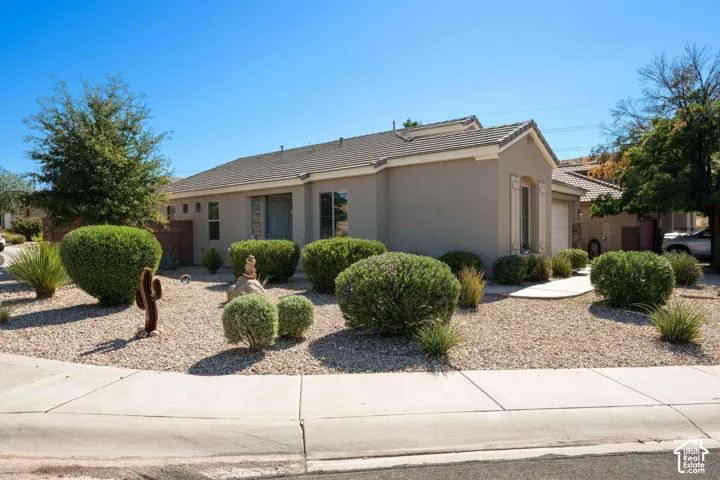 Stucco exterior with a tiled roof, featuring xeriscaped front yard with decorative gravel and mature shrubbery