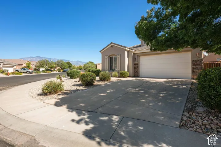 Stucco exterior with stone accents, a two-car garage, concrete driveway, and established desert landscaping